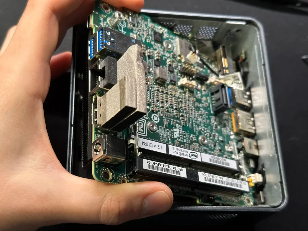 Витягнута материнська плата Intel NUC8 в руках, видно EMI прокладку